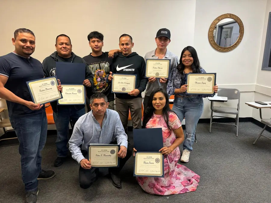 Ocho graduados de ICC&nbsp;Center sosteniendo sus certificados en el salón de clases