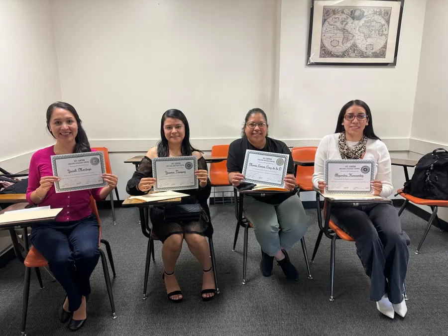 Cuatro graduadas sentadas en sus pupitres mostrando sus certificados de ICC&nbsp;Center